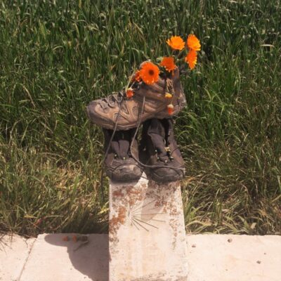 Wandelschoenen op een camino paaltje gevuld met bloemen