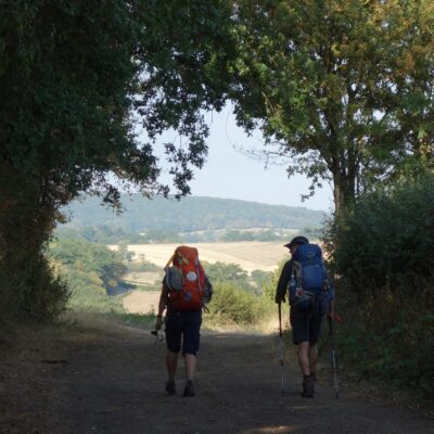 Twee pelgrims op pad met bomen lopen richting zonnig dal