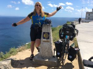 Bicigrina met haar fiets bij een caminomijlpaal aan de kust