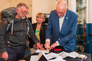 Peter Hesseling zet het eerste stempel in het paspoort van Peter ter Wal, Jeanine Colet-Oosterhuis kijkt toe