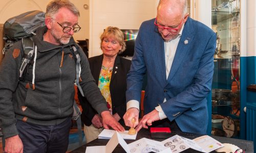Peter Hesseling zet het eerste stempel in het paspoort van Peter ter Wal, Jeanine Colet-Oosterhuis kijkt toe